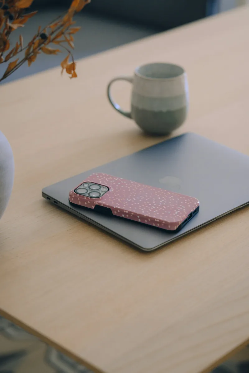 Pink phone case beside a laptop and mug